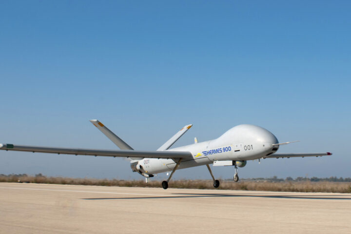 White Hermes 900 UAV on a runway with landing gear down, clear blue sky above.