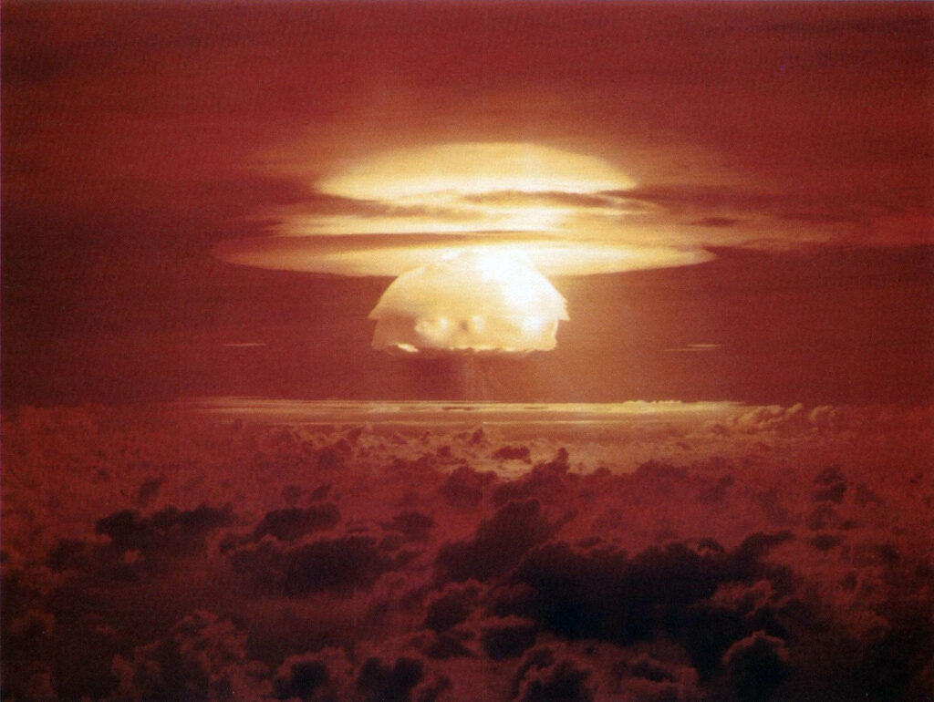 Nuclear explosion mushroom cloud rising above clouds at sunset over a dark horizon sea of clouds.