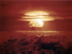 Nuclear explosion mushroom cloud rising above clouds at sunset over a dark horizon sea of clouds.