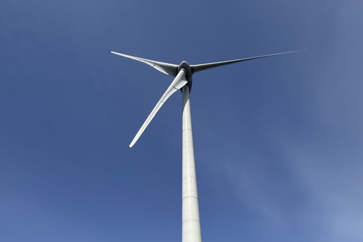Wind turbine viewed from below with blue sky background and three blades extending outward
