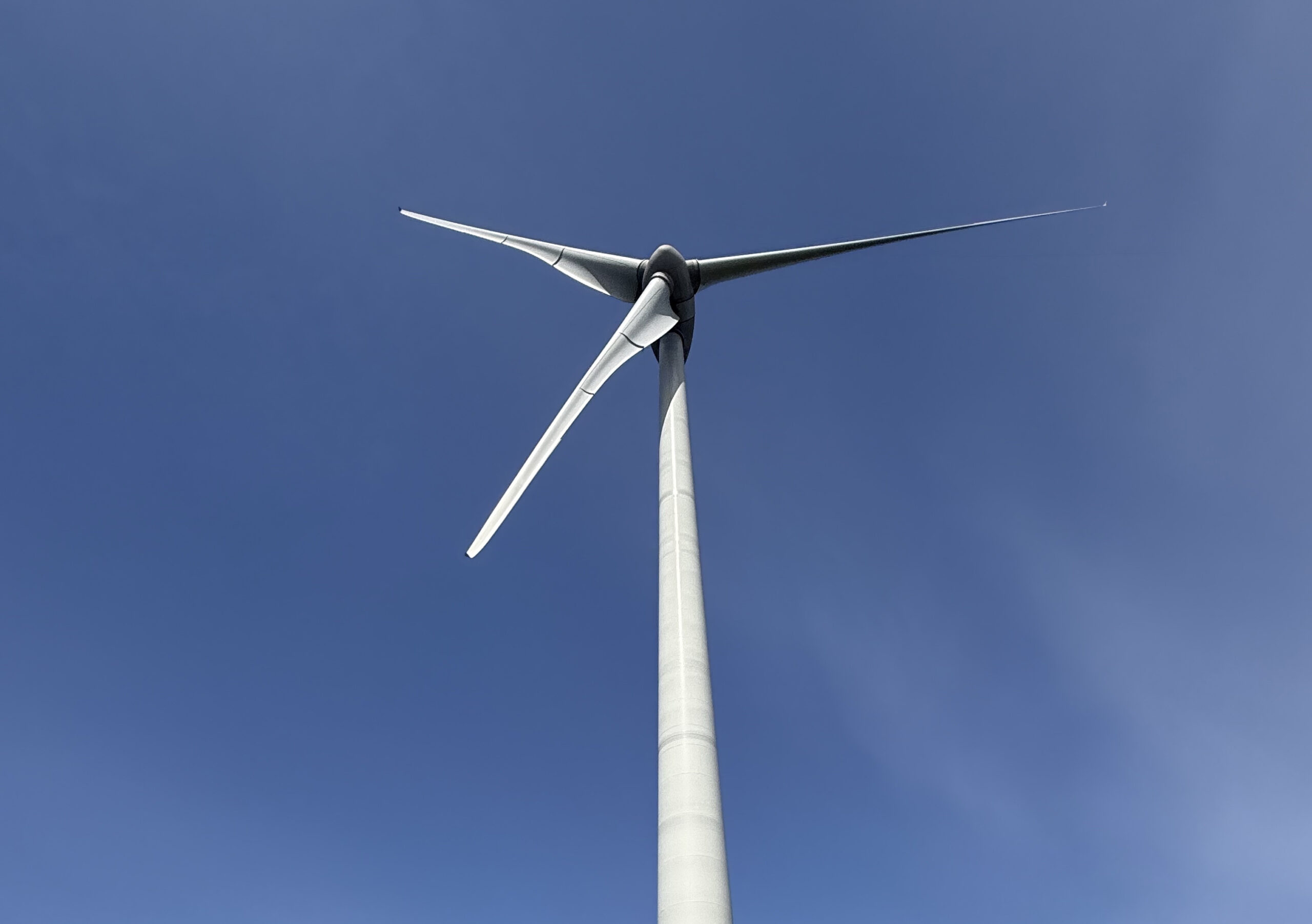 Wind turbine viewed from below with blue sky background and three blades extending outward