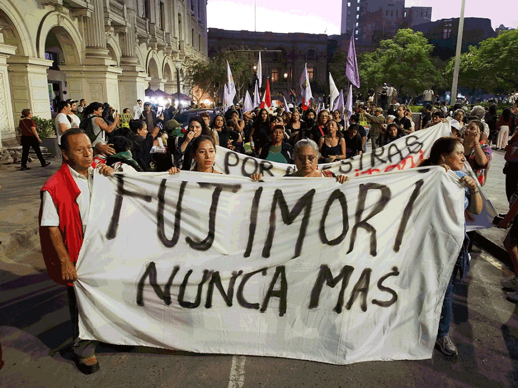 Protesters hold a large white banner reading 'NUNCA MAS' at a night march on a city street with a historic building in the background.