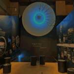 Large circular wall display resembling an eye with a blue-green center, timeline labels around the edge in a dark museum gallery with text panels nearby.