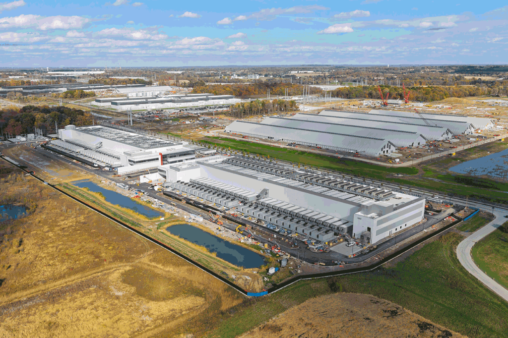 Aerial view of a large industrial complex with multiple white warehouses under construction, cranes, and surrounding fields.