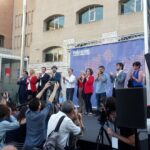Speakers on a stage clap as photographers in front capture the event near a blue Fearless Cities banner in Barcelona.