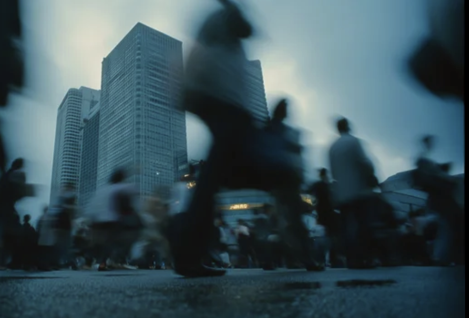 Blurred pedestrians move through a busy city plaza with tall skyscrapers in the background, conveying urban bustle.