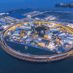 Aerial view of a circular waterfront shopping complex lit up at night on a man-made island.