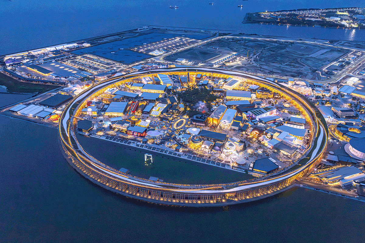 Aerial view of a circular waterfront shopping complex lit up at night on a man-made island.